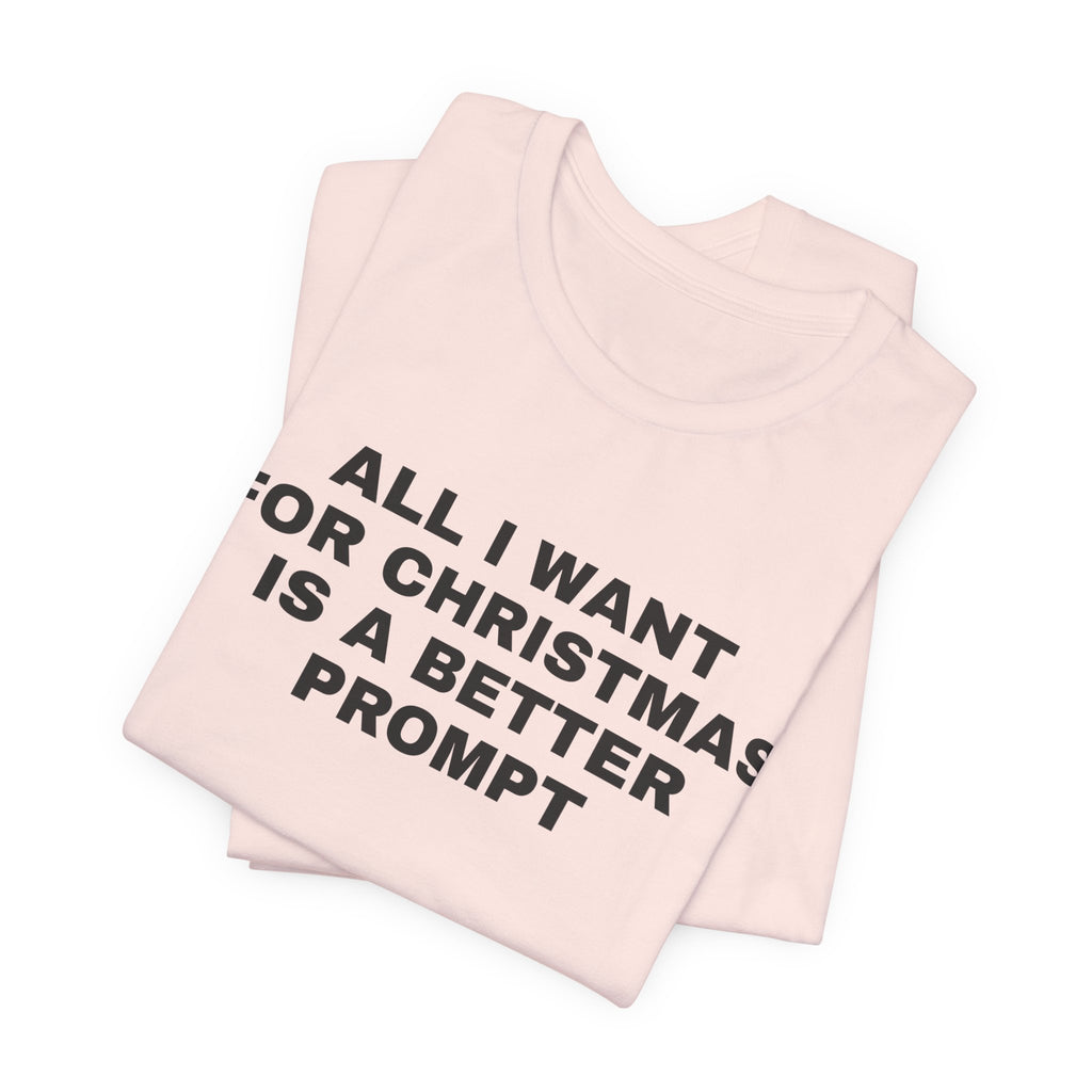 Soft pink t-shirt printed with 'All I want for Christmas is a better prompt', folded
