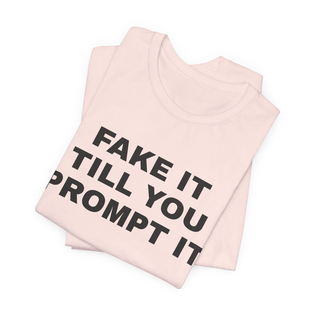 Soft pink t-shirt printed with 'Fake it till you prompt it', folded
