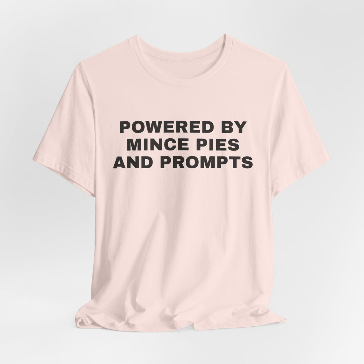 Soft pink t-shirt printed with 'Powered by Mince Pies and Prompts'