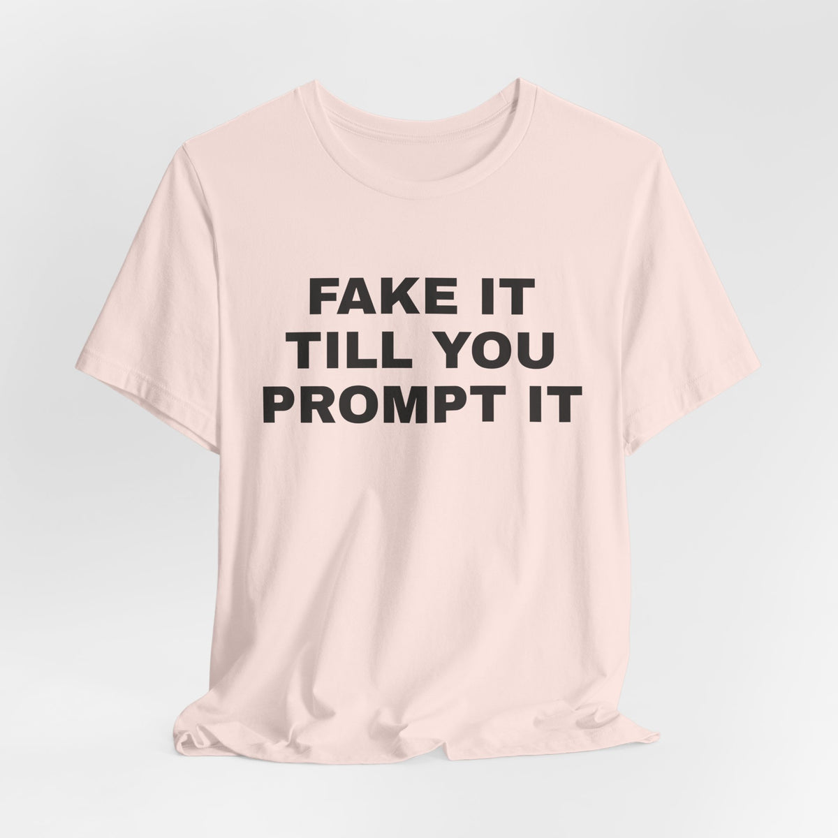 Soft pink t-shirt printed with 'Fake it till you prompt it'