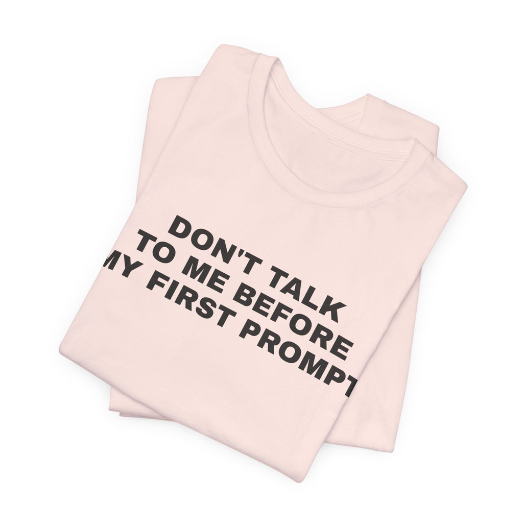 Soft pink t-shirt printed with 'Don't talk to me before my first prompt', folded